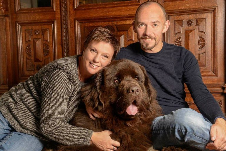 Twee mensen zitten met een grote bruine hond voor een houten deur