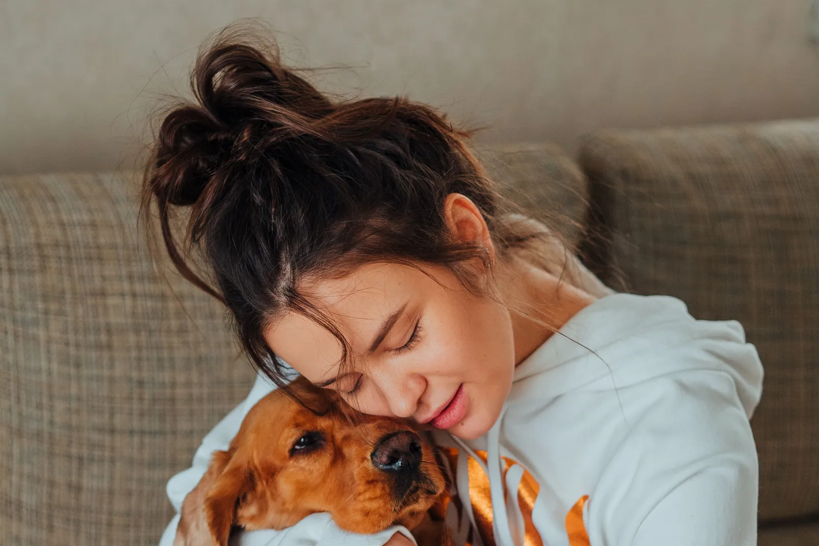 Vrouw omhelst haar bruine hond op de bank