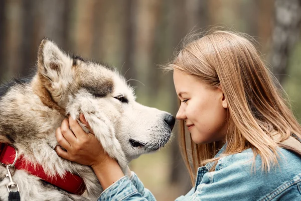 Meisje naast een grote grijs-witte hond in het bos