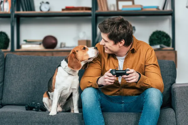 Man zit met een hond op de bank en houdt een spelcontroller vast